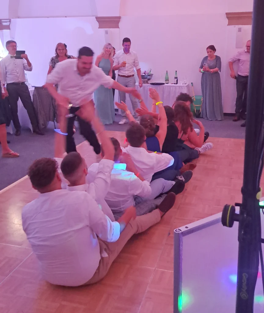 Hochzeitsgäste sitzen bei einem gemeinsamen Partyspiel hintereinander auf der Tanzfläche