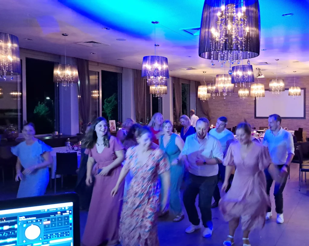Hochzeitsgäste tanzen in einem Festsaal mit blauer Beleuchtung und Kronleuchtern