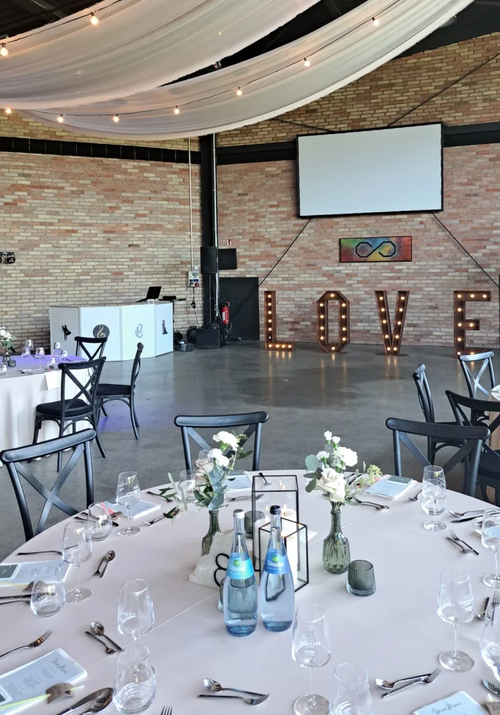 Festlich gedeckte Hochzeitstische in einem Saal mit Steinwänden und weißen Stoffbahnen